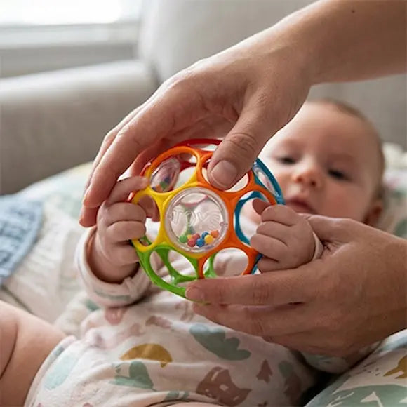 bébé allongé tient balle sensorielle bebe aidé mains parent