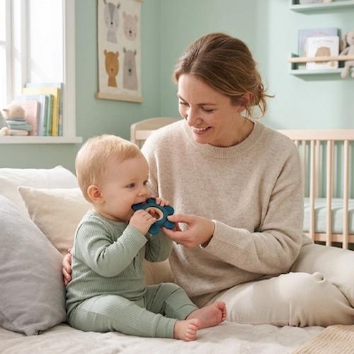 bebe assis lit mordille anneau de dentition maman surveille