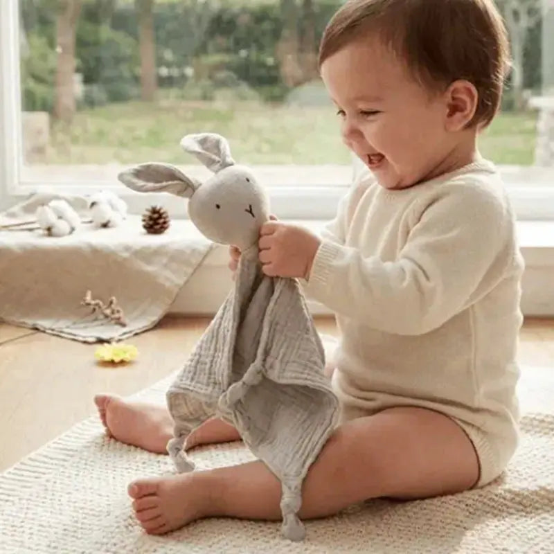 bébé assis regarde doudou lapin gris tendrement