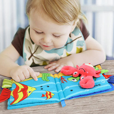 bebe assis regarde livre bebe en tissus