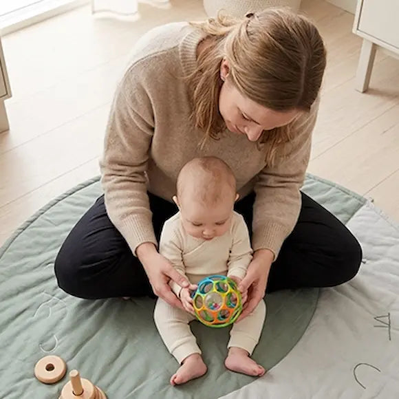 bébé assis tapis vert avec maman tient balle sensorielle bebe