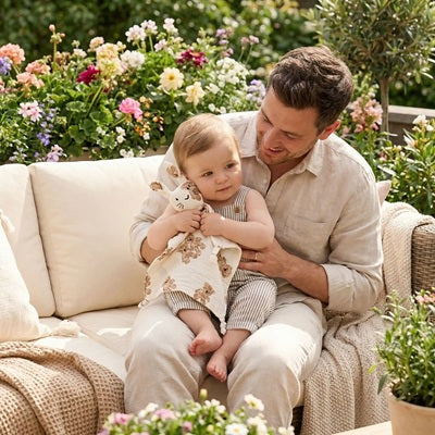 bebe caline doudou naissance assis genou papa canape jardin fleuri