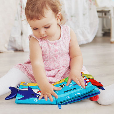 petite fille assise regarde livre bebe en tissus